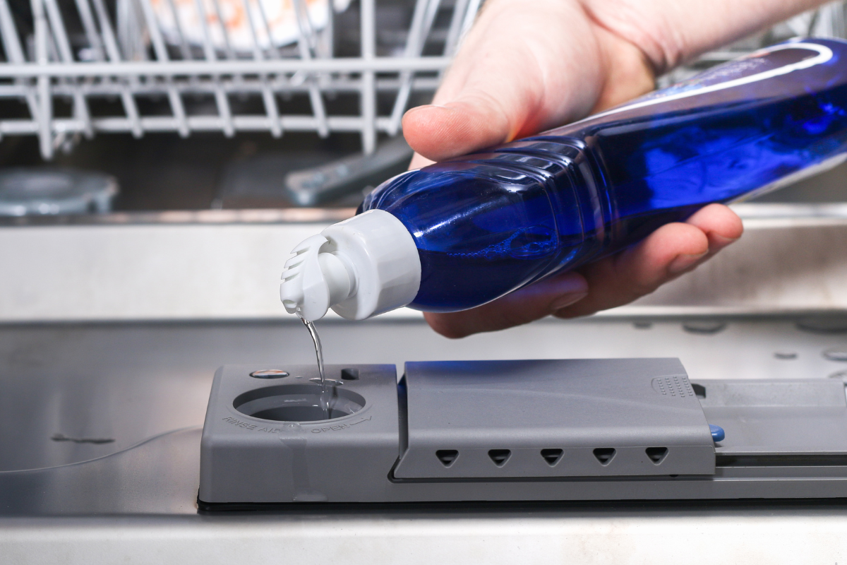 Homeowner filling the rinse aid dispenser in a dishwasher door to prevent cloudy dishes